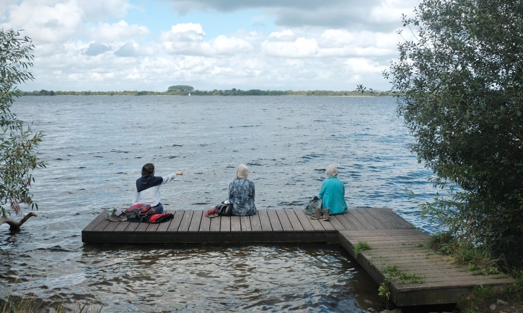 Drie dames op leeftijd genieten van het uitzicht over het water, op anderhalve meter van elkaar.