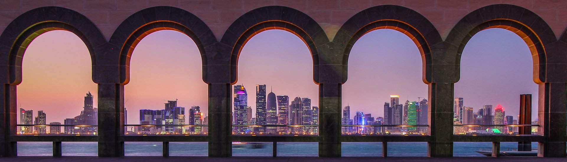skyline van Doha in Qatar gezien door een galerij van zuilen en bogen.