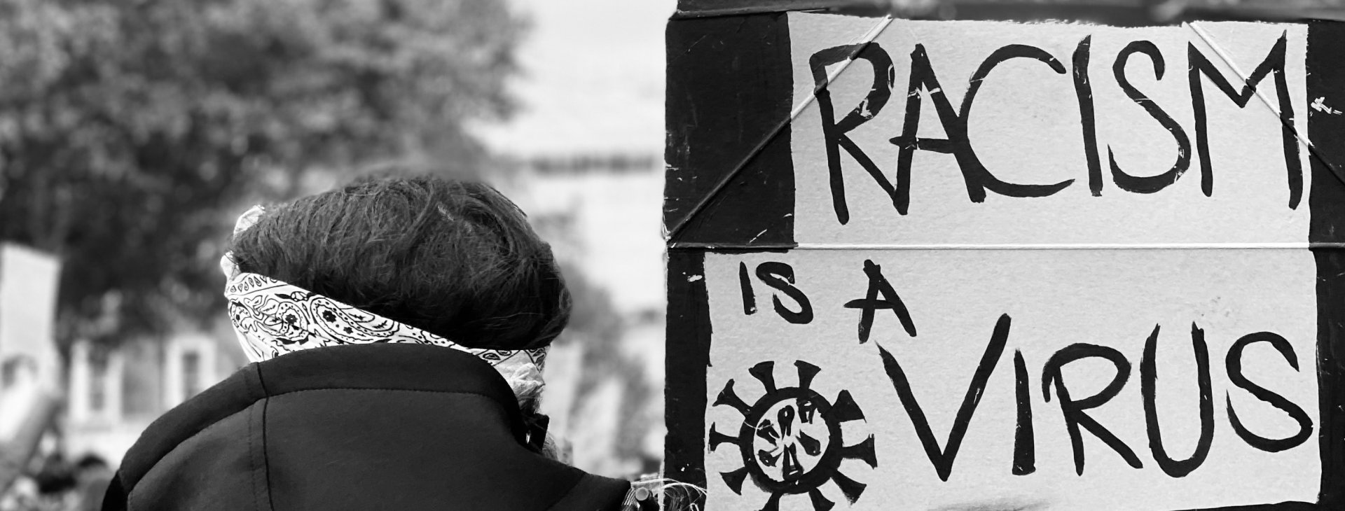 Een vrouw draagt een bord met de tekst 'Racism is a virus'.