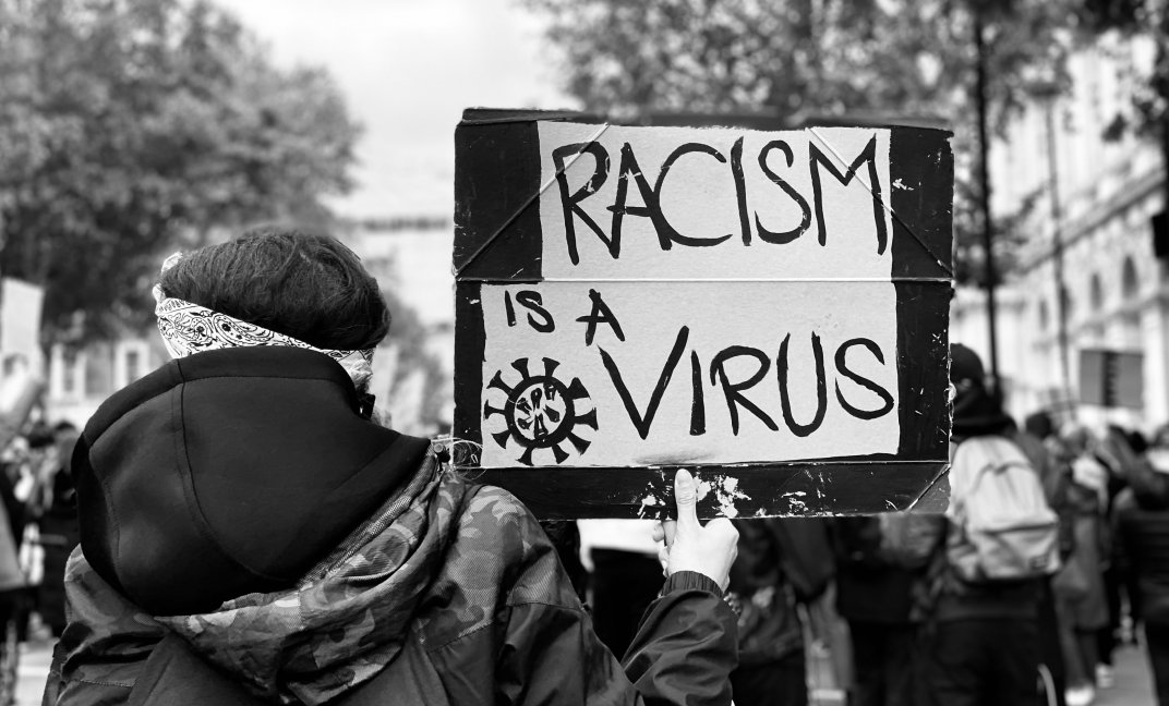 Een vrouw draagt een bord met de tekst 'Racism is a virus'.