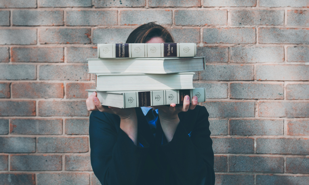 Vrouw met een stapel boeken voor haar gezicht