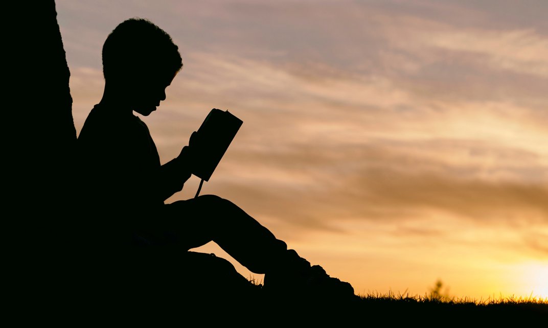 Foto van een kind dat een boek leest in de avondzon. (Foto: Unsplash.com | Aaron Burden)