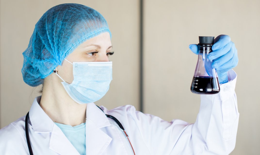 Een vrouwelijke onderzoeker kijkt naar een fles met vloeistof in een laboratorium.