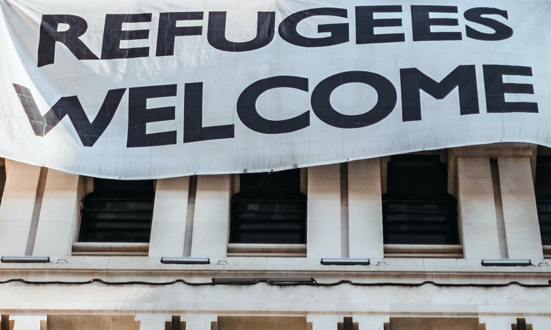 Spandoek met de tekst 'Refugees Welcome' hangt aan een gebouw.