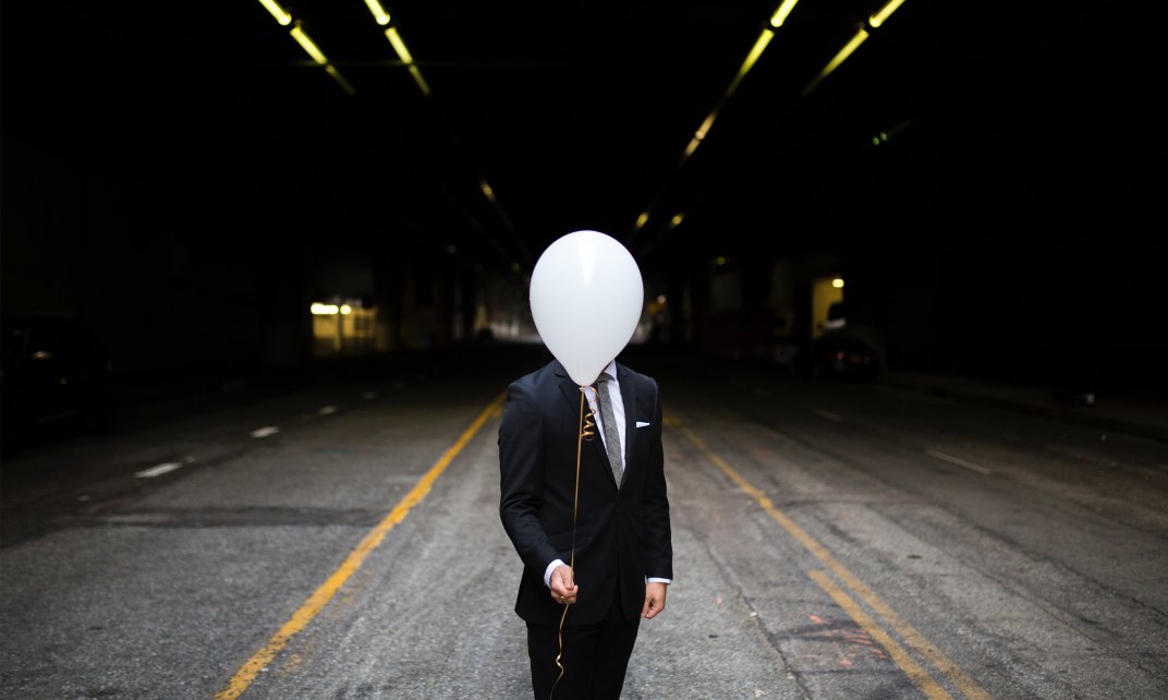 Het hoofd van een man wordt ontrokken aan het zicht door een witte ballon (Foto: Unsplash.com | Andrew Worley)